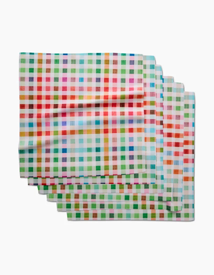 Four colorful Woven Spring Plaid Dinner Napkins by Pascale Dilger, featuring red, green, blue, orange, and yellow stripes, are stacked on a white background. Made from soft Geosuede fabric with recycled materials.