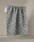 The "You Make Me Happy" towel by Kelsi Fullmer, featuring a gray ultra-absorbent fabric with white smiley faces, hangs on a clothesline against a plain beige background.