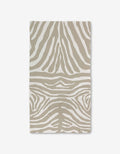 The GEOMETRY Zen Zebra bath towel, featuring a beige and white zebra stripe pattern and crafted with Geoweave technology for superior absorbency, is shown flat on a white background.