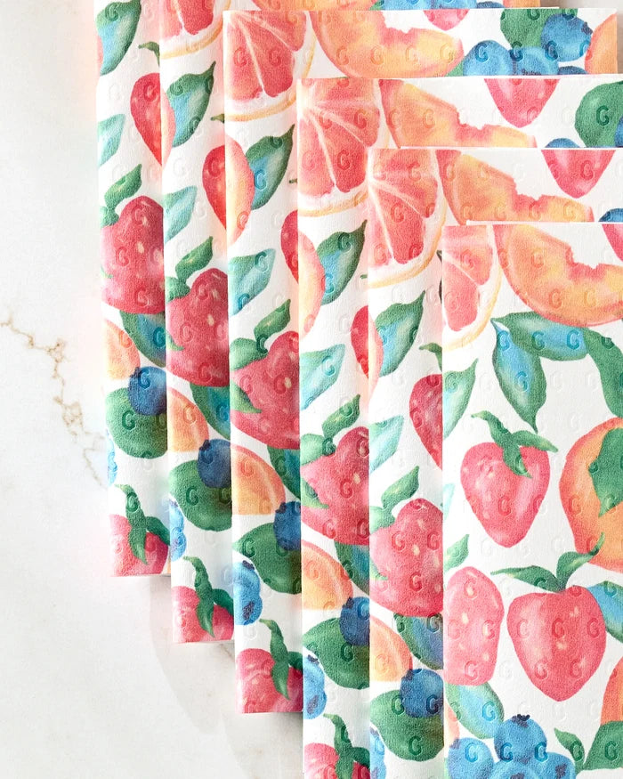 Five eco-friendly Zesty Life paper towels by Aubrey Fairchild, each featuring vibrant strawberry, blueberry, and peach illustrations, are displayed fanned-out on a white marble surface.