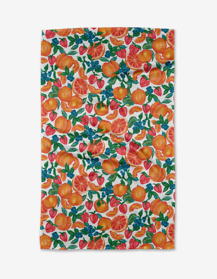 The Zesty Life tea towel by Aubrey Fairchild showcases a lively print of oranges, strawberries, and green leaves on white, expertly made from recycled materials.
