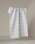 The Ziggy Floral tea towel by Elizabeth Edwards, made from recycled materials, displays blue vertical lines and red-orange asterisks and hangs from a clothesline against a neutral background.