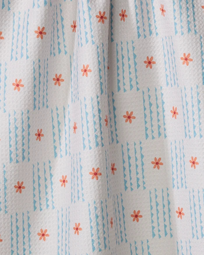 A close-up of the Ziggy Floral tea towel by Elizabeth Edwards, featuring small orange flowers and blue geometric stripes in a grid on white. Its slightly dimpled texture highlights its ultra-absorbent quality.