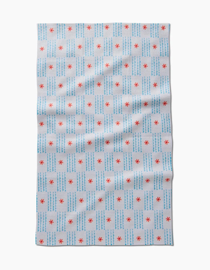 The Ziggy Floral by Elizabeth Edwards is a white tea towel with blue dashed grid lines and small red stars at some intersections, made from recycled materials. It’s shown flat with slight wrinkles.