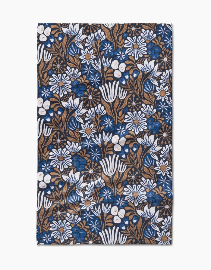 The Zillia Tea Towel by Amy MacCready features a dense floral pattern of white and blue flowers, brown stems, and green leaves on recycled Geoweave fabric with a dark background.