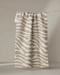 The Geometry Zira Tan tea towel, featuring beige and white zebra stripes, hangs on a thin clothesline against a softly lit neutral background.