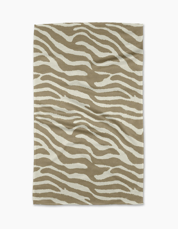 The Zira Tan tea towel by Geometry features a white zebra stripe pattern on rectangular beige fabric, displayed flat on a white background.